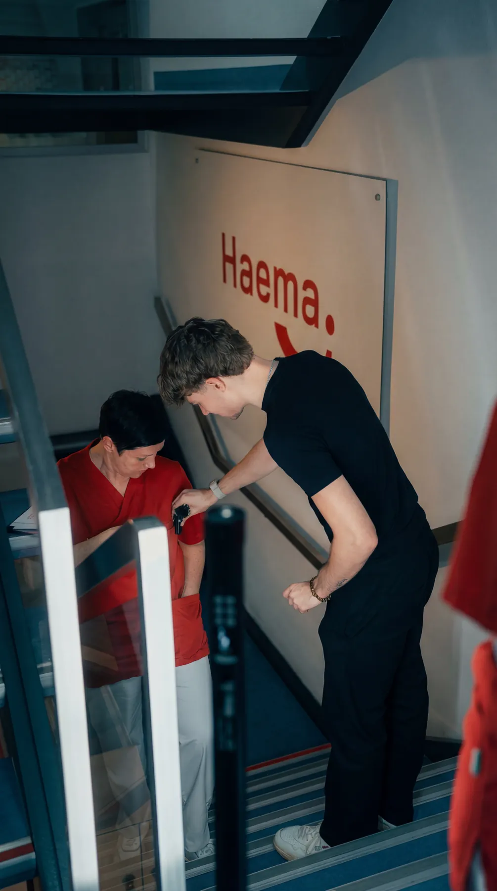 Absprache mit einer Mitarbeiterin im Treppenhaus bei Haema, an der Wand das Haema-Logo